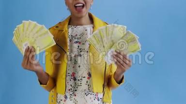 高兴兴奋的非裔美国妇女，在蓝色背景的黄色夹克上炫耀金钱，说上帝保佑